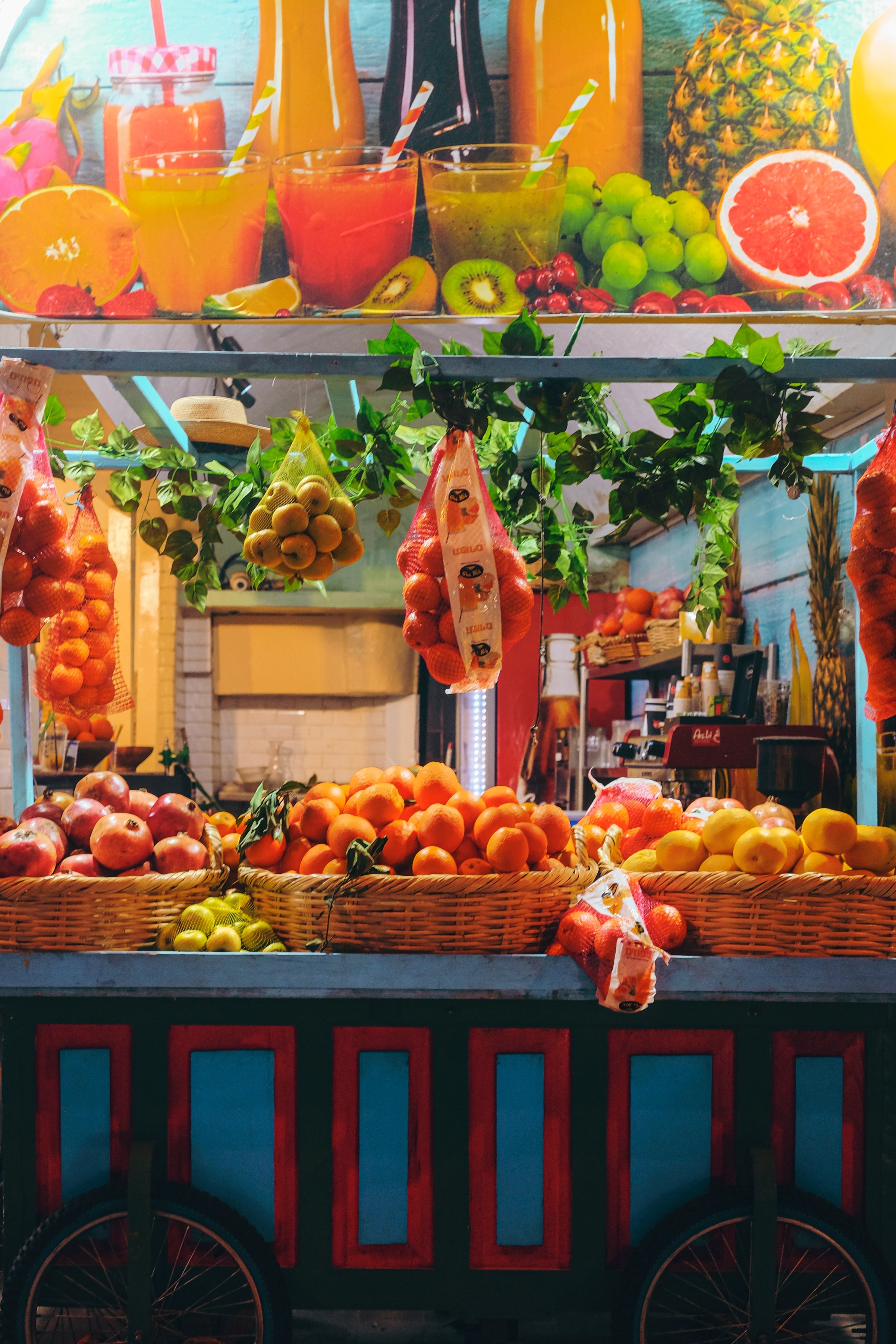 A colourful fruit cart on wheels, you can see large baskets of oranges, lemons and pomegranates.