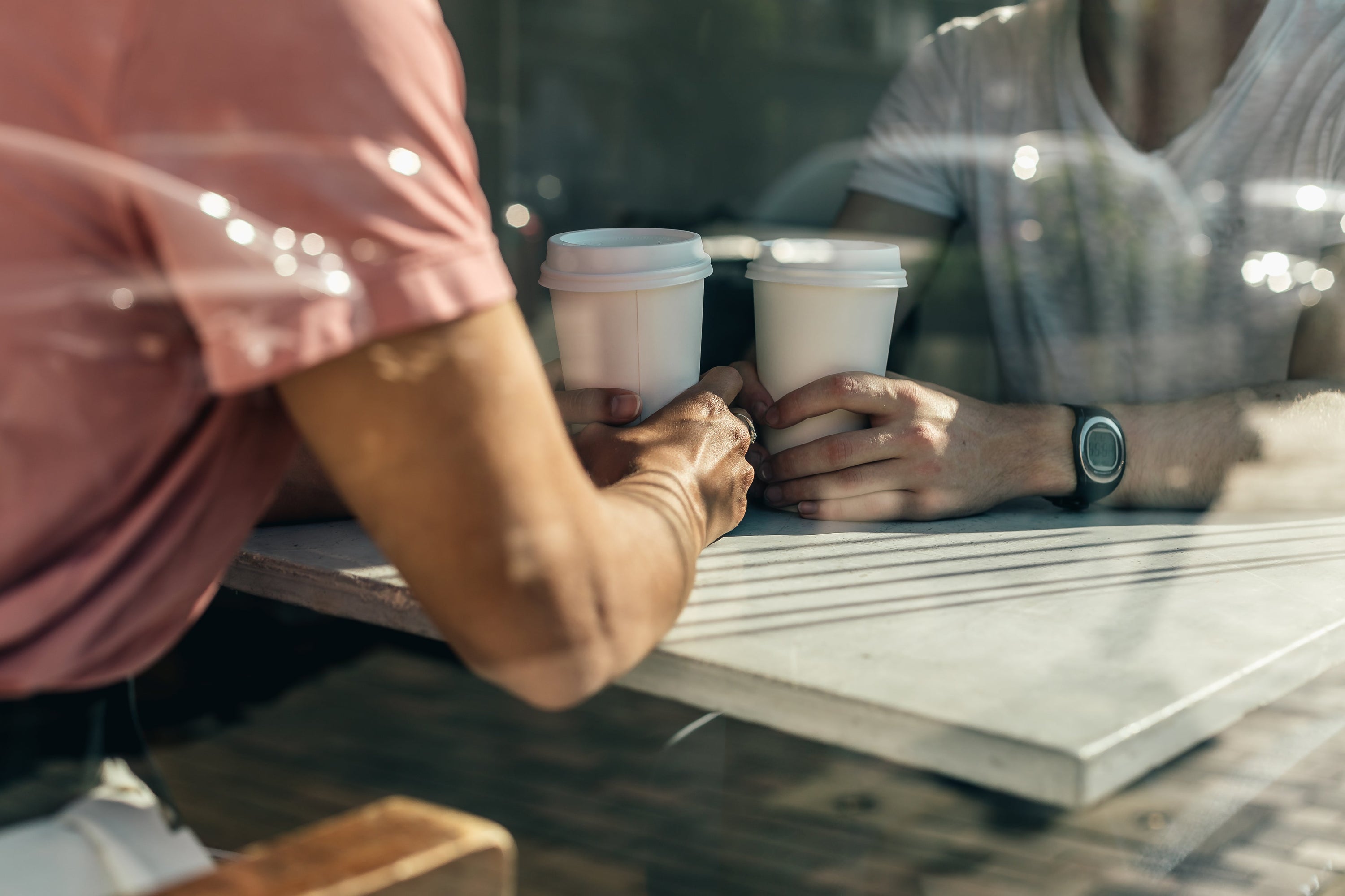 Two people sit at a table inside a coffee shop, coffee in hand as they reminisce over their past adventures together.