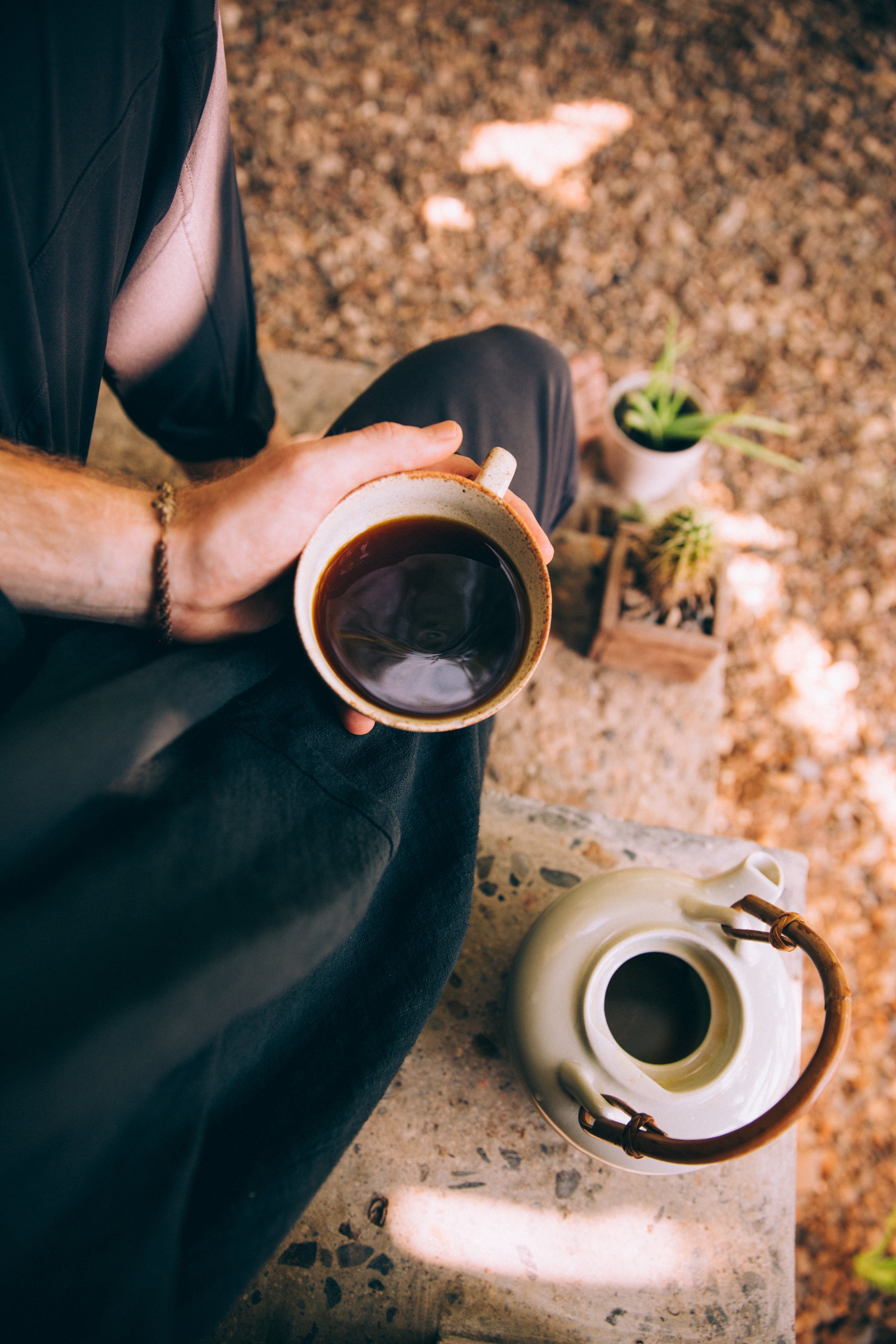 Sitting on a step with nature for company, a young man sits and drinks black coffee.