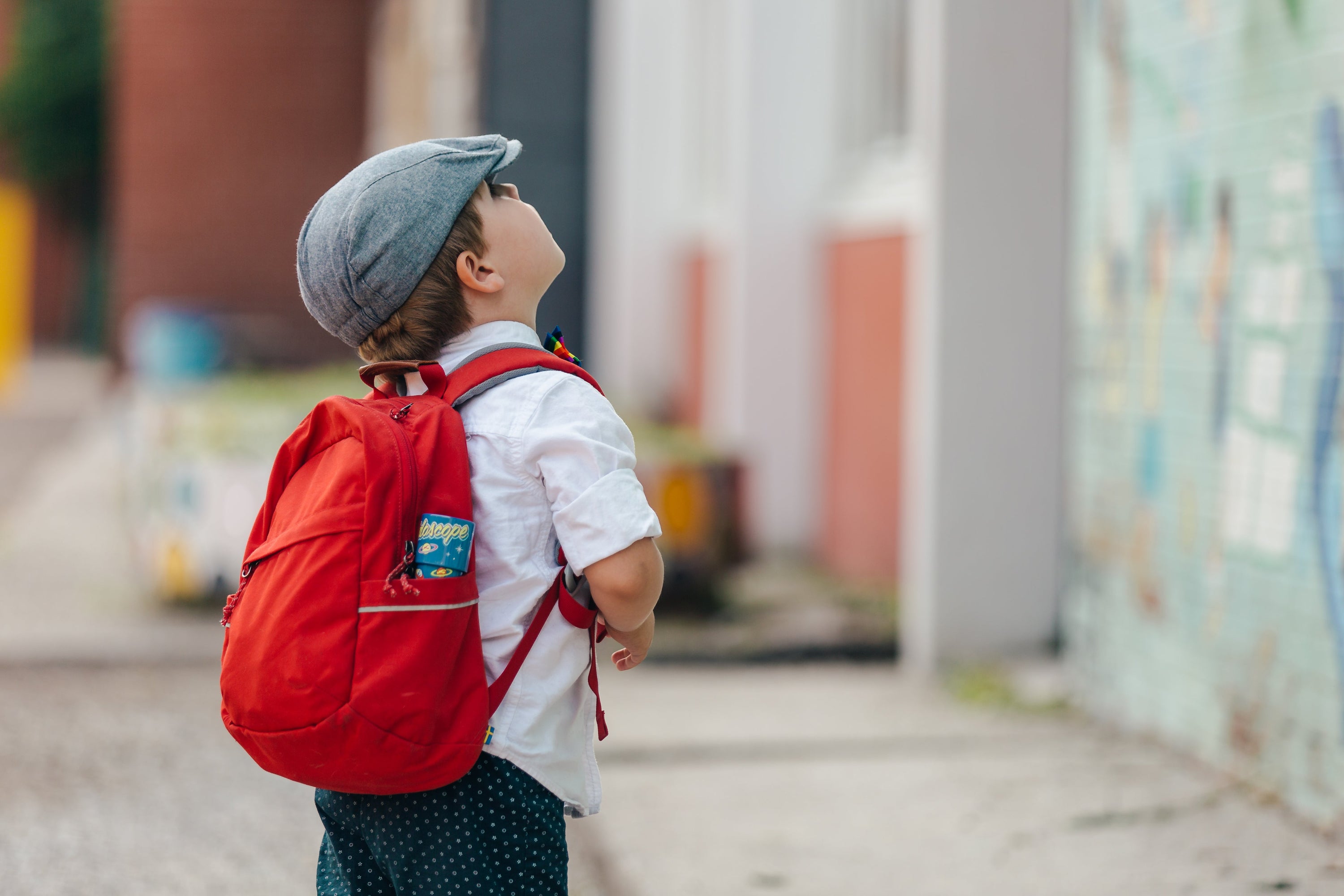 A young boy wearing his backpack is gazing up at his new school before his first day.