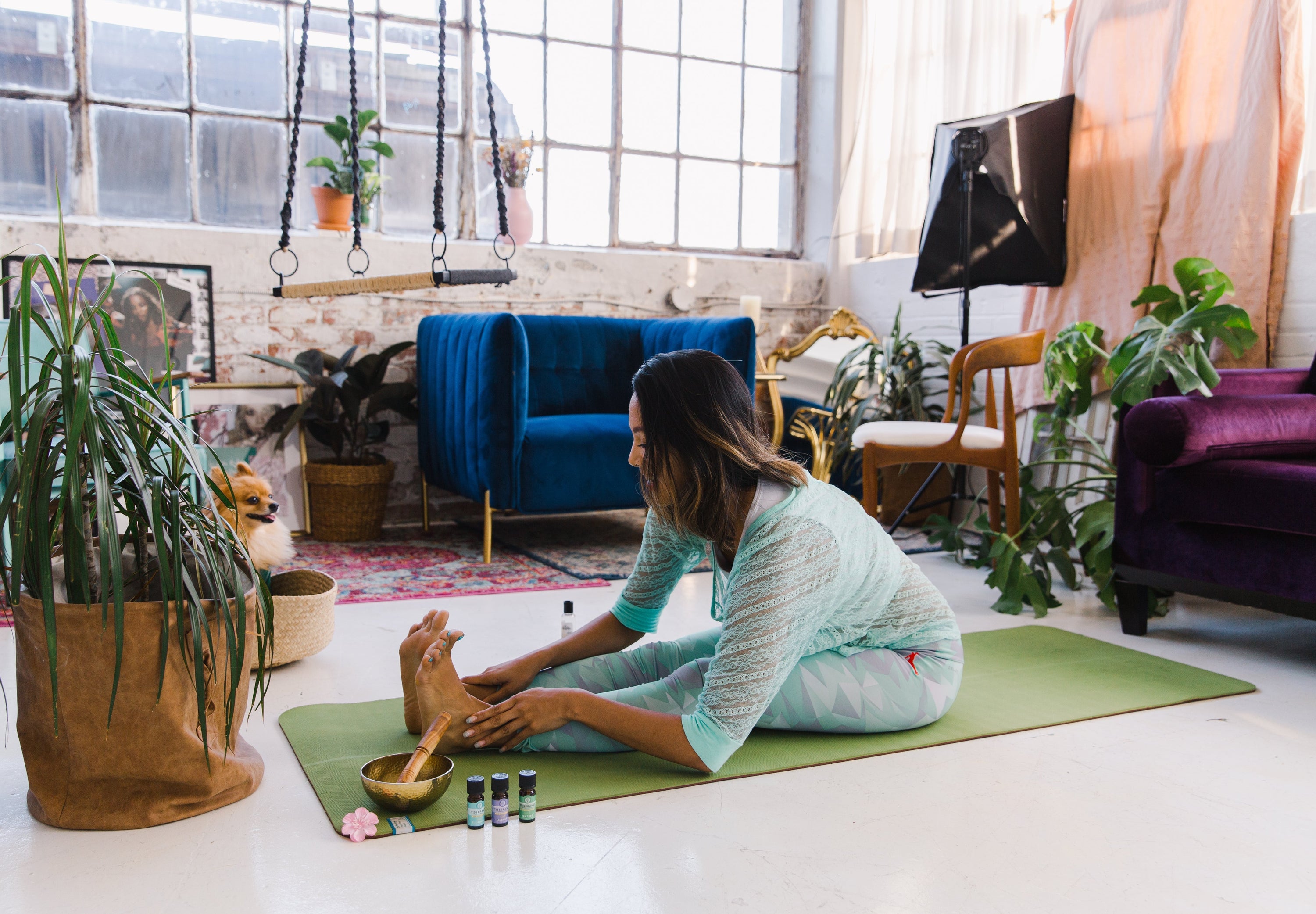 A woman stretches and gets ready to practice yoga while a little dog watches.