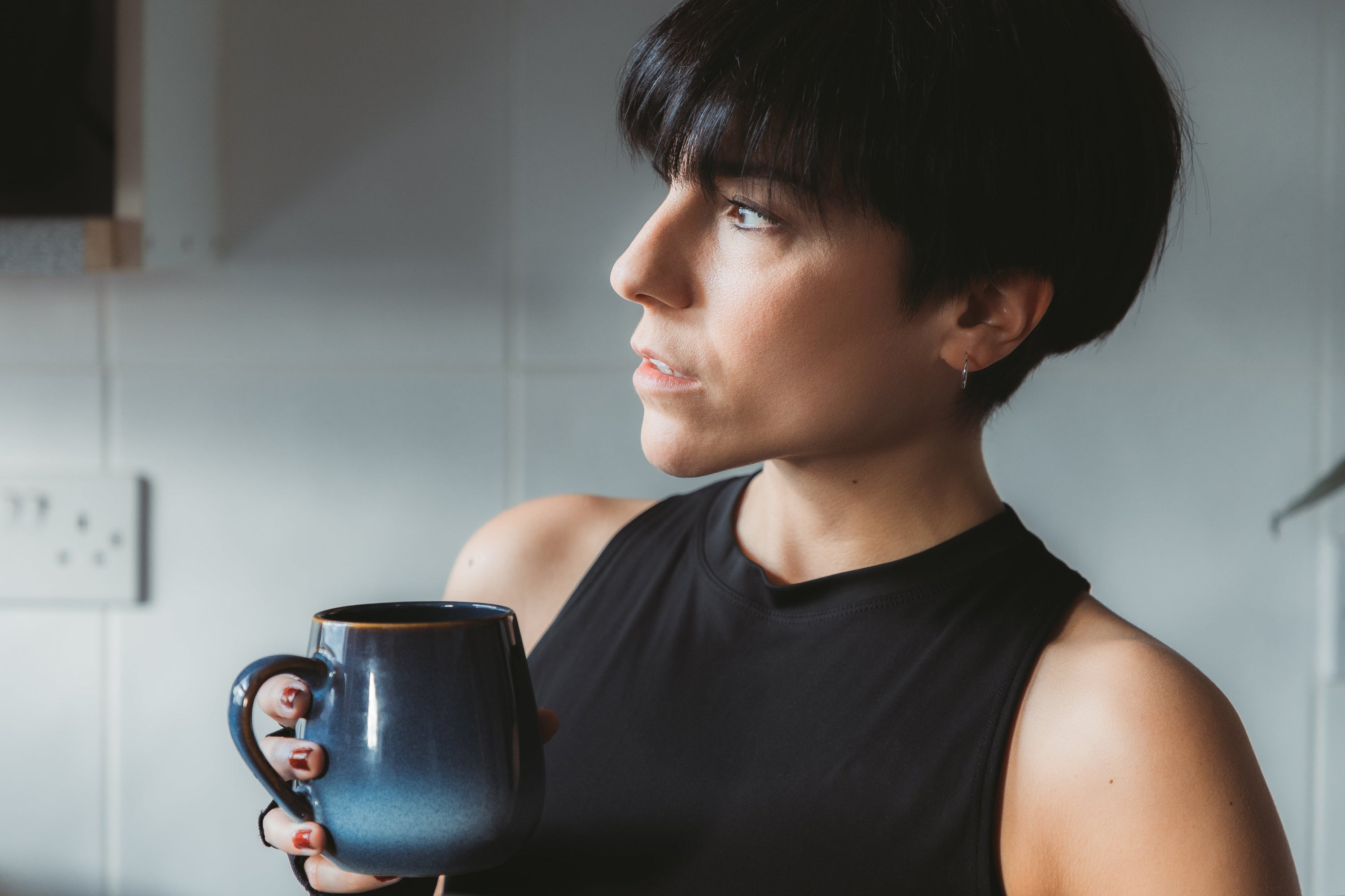 Women with short black hair holds a blue mug and looks to the left of the frame.Women with short black hair holds a blue mug and looks to the left of the frame.