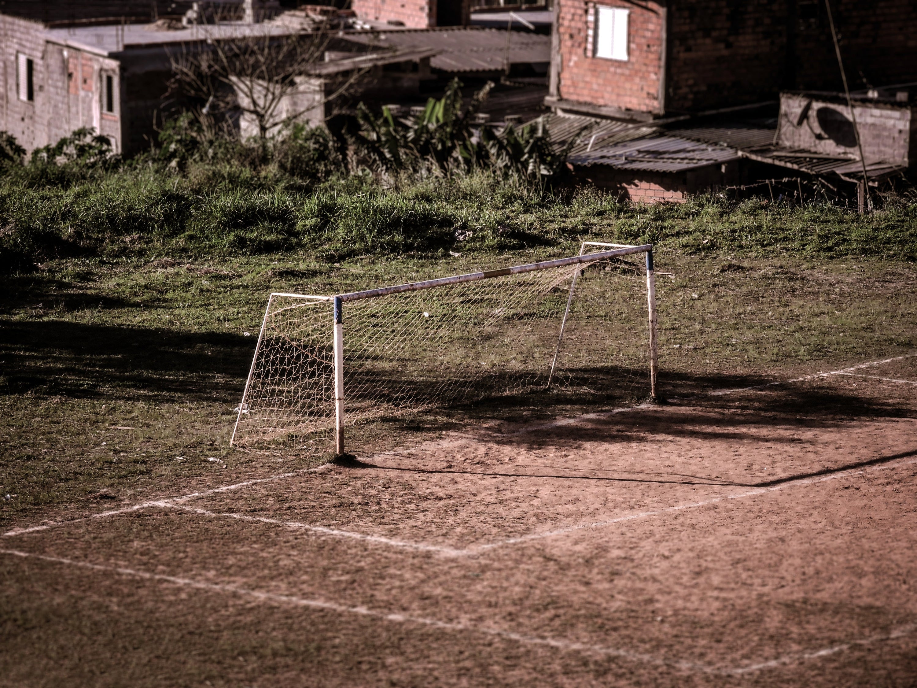 An empty sports net with green grass behind it and brown dirt with white lines in front of it