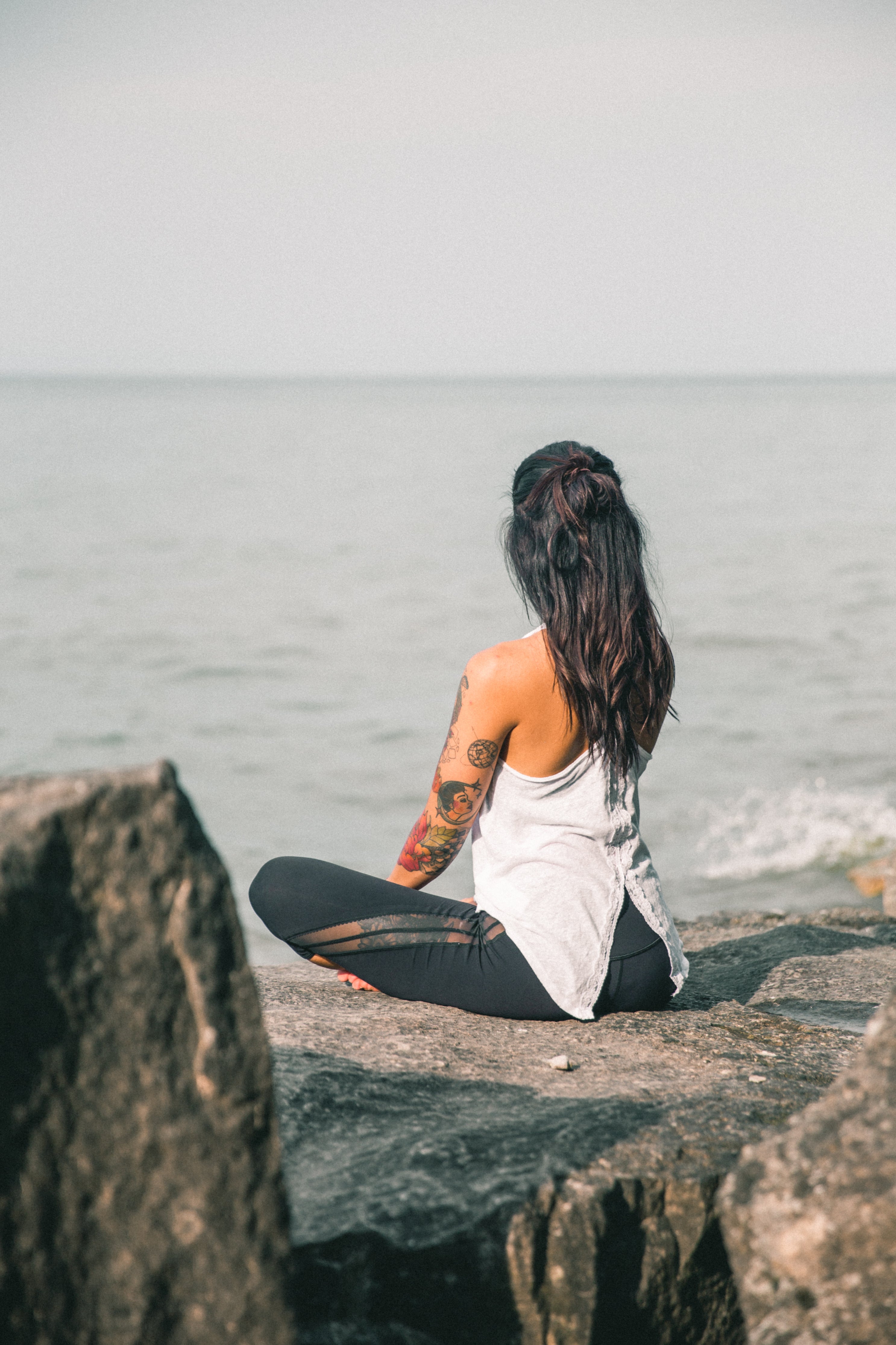 A woman sits cross-legged on a large rock overlooking the sea.