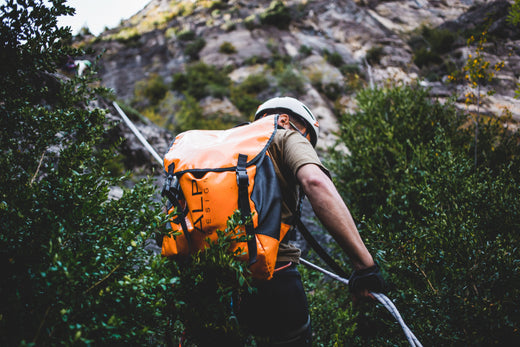 Climber rappelling down a mountain with helmet and gear in backpack.