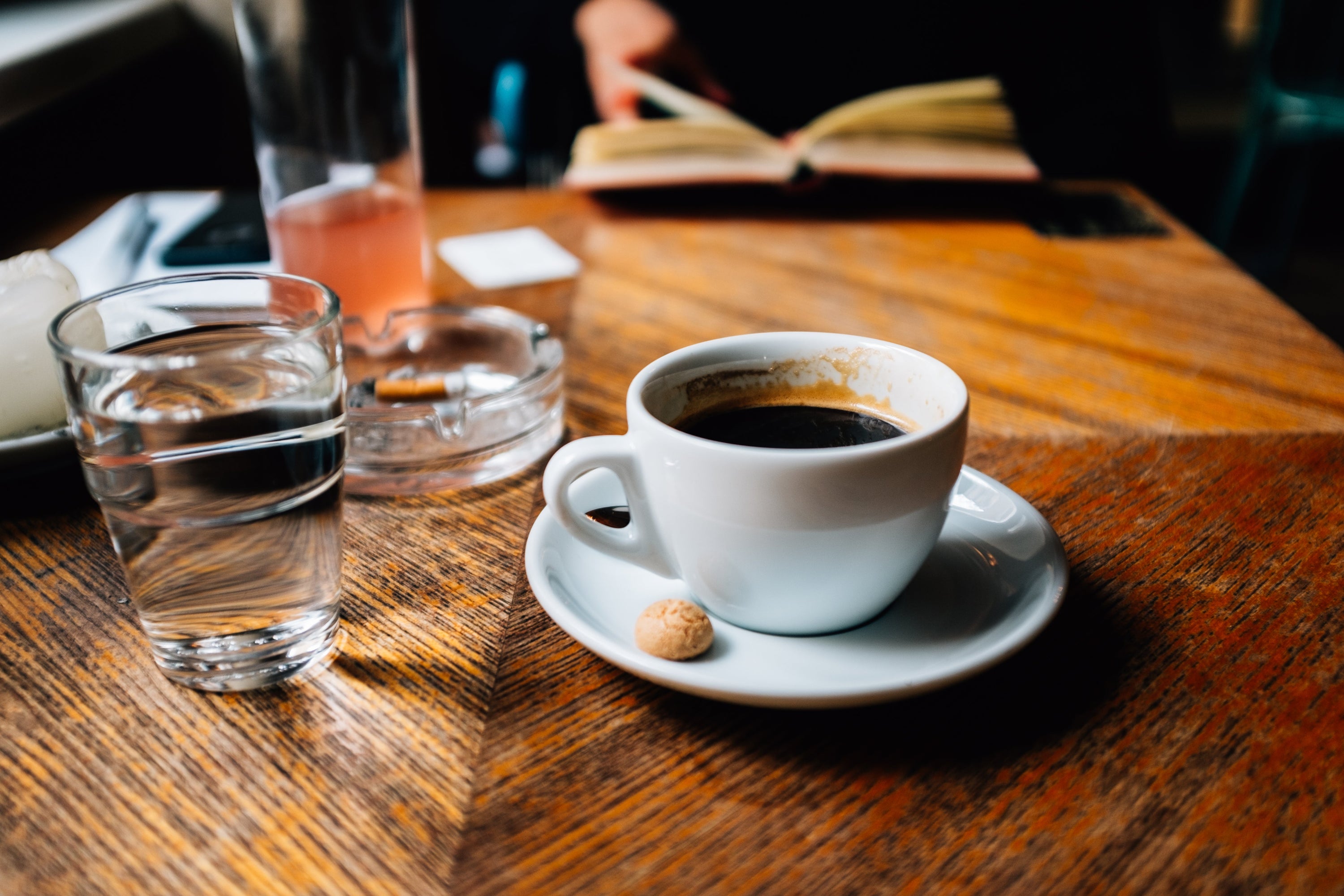 A dark cup of joe sits in a classic white cup with serving plate upon a cluttered tabletop