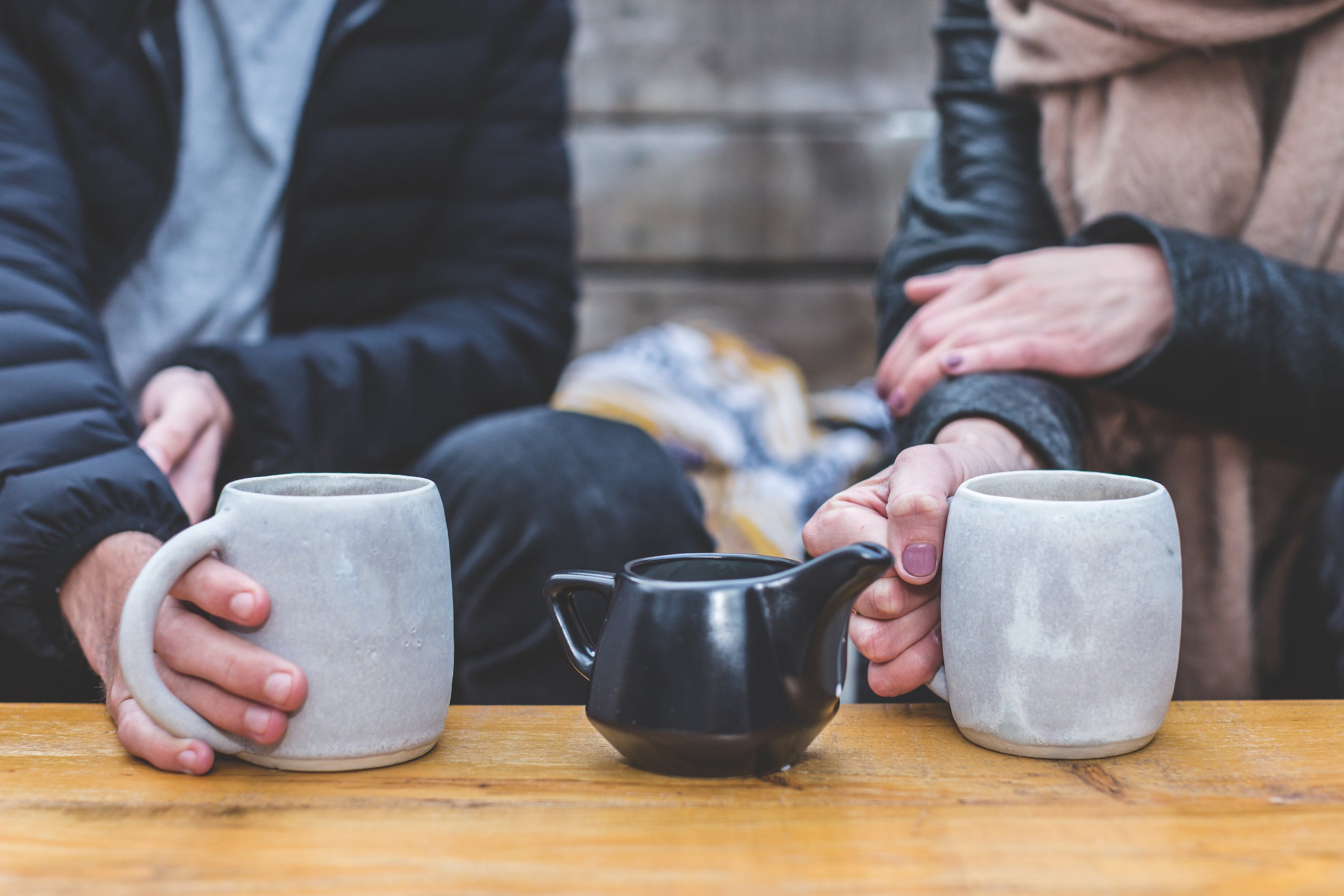 Close up of a man and woman holding coffee mugs on a table with creamer container in the middle.