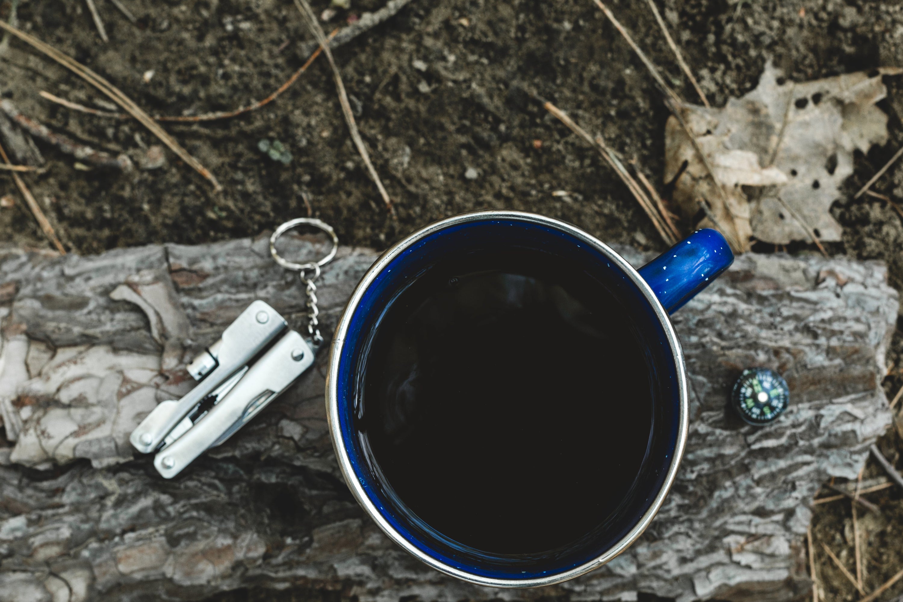 Flatlay of coffee cup, compass & knife. Ready for anything in the great outdoors.