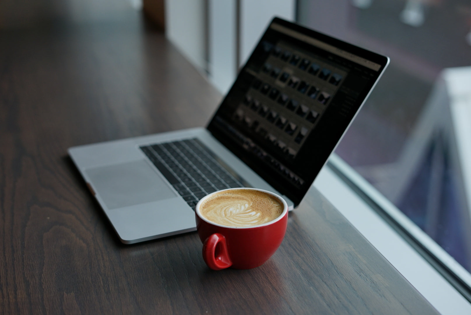 A laptop computer sits on a table with a beautifully made cappuccino beside it.