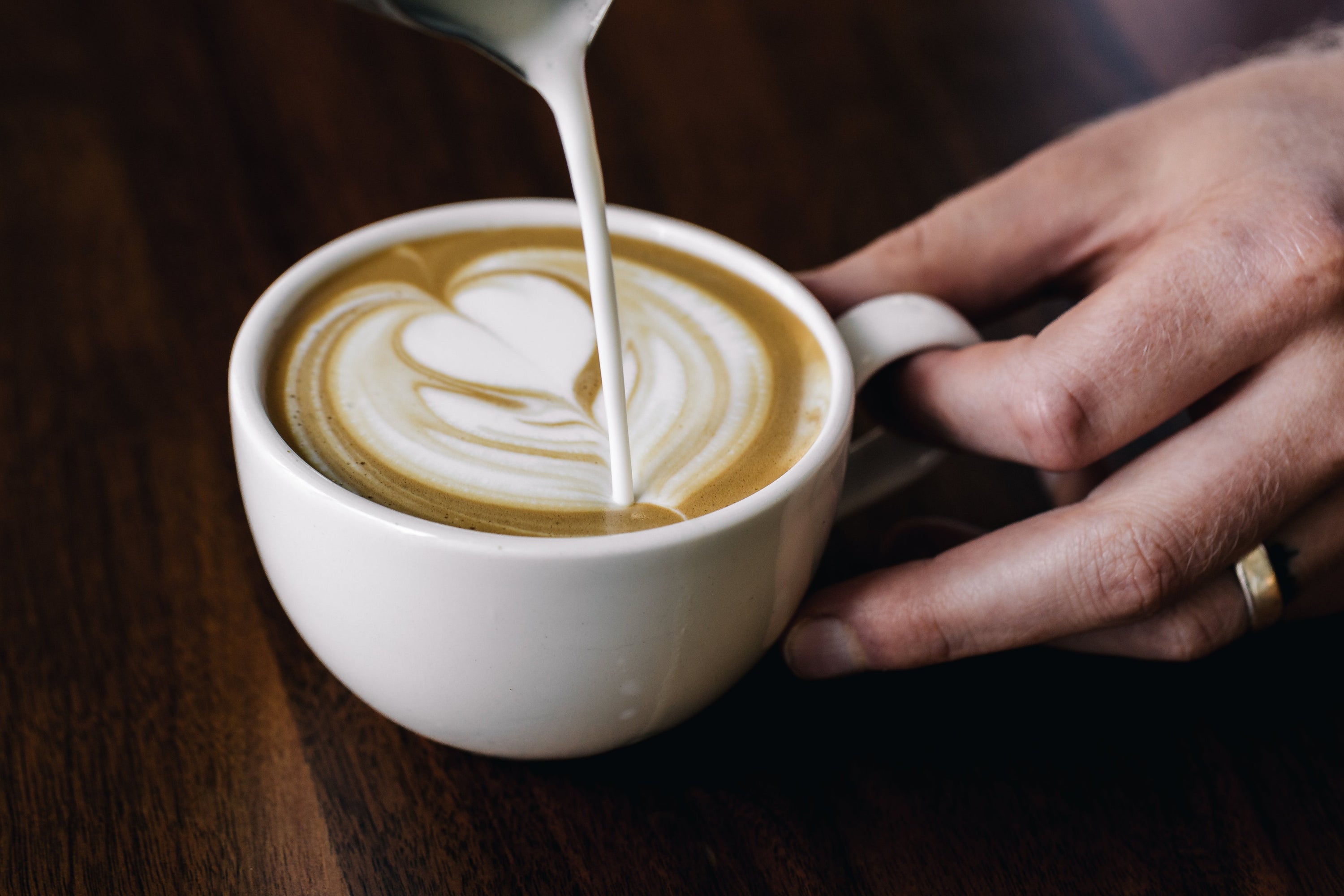 A cafe barista pours frothed milk into an espresso to create a heart-shaped on top of the coffee.