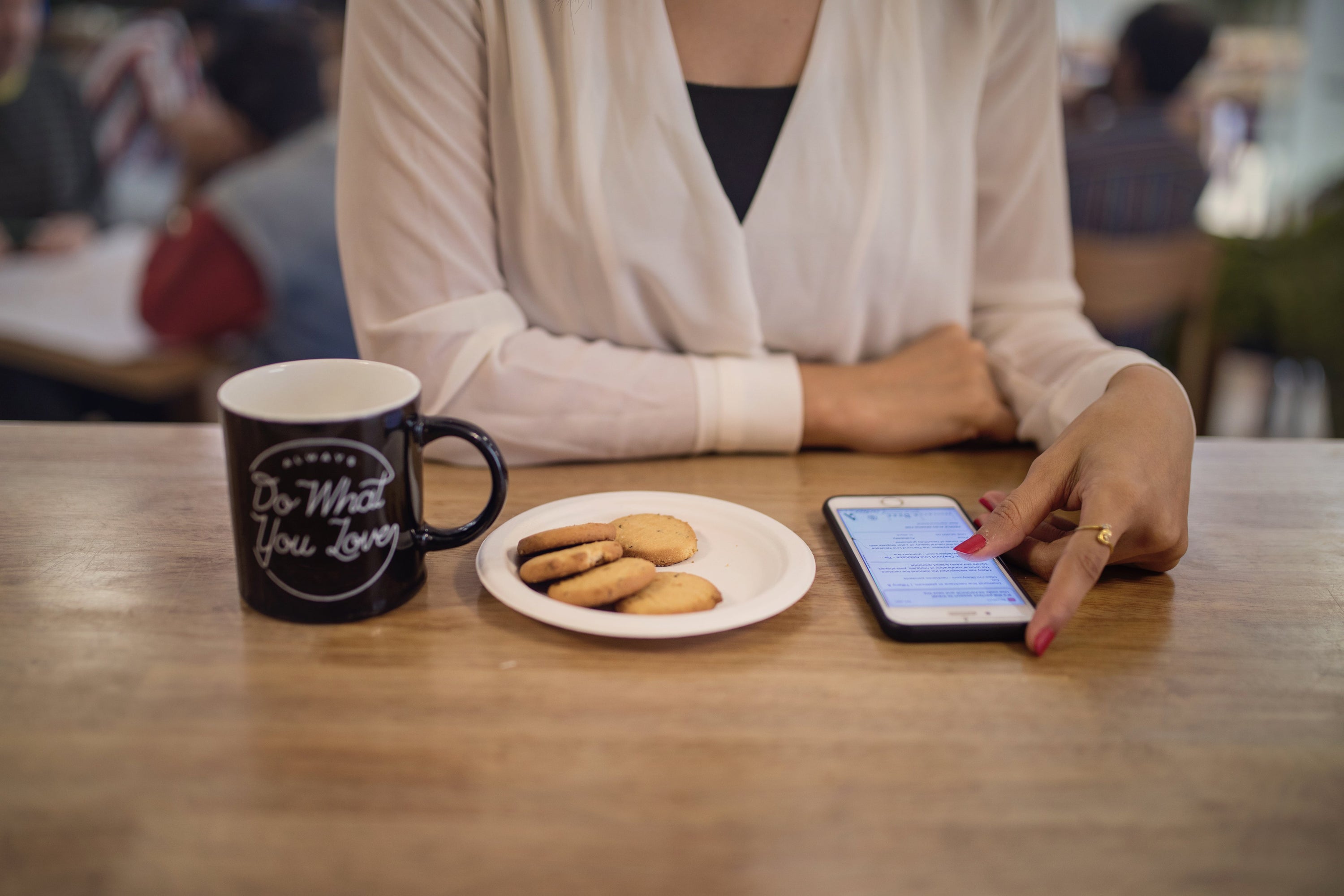 Coffee cup and cookies on a table in front of woman viewing her smartphone