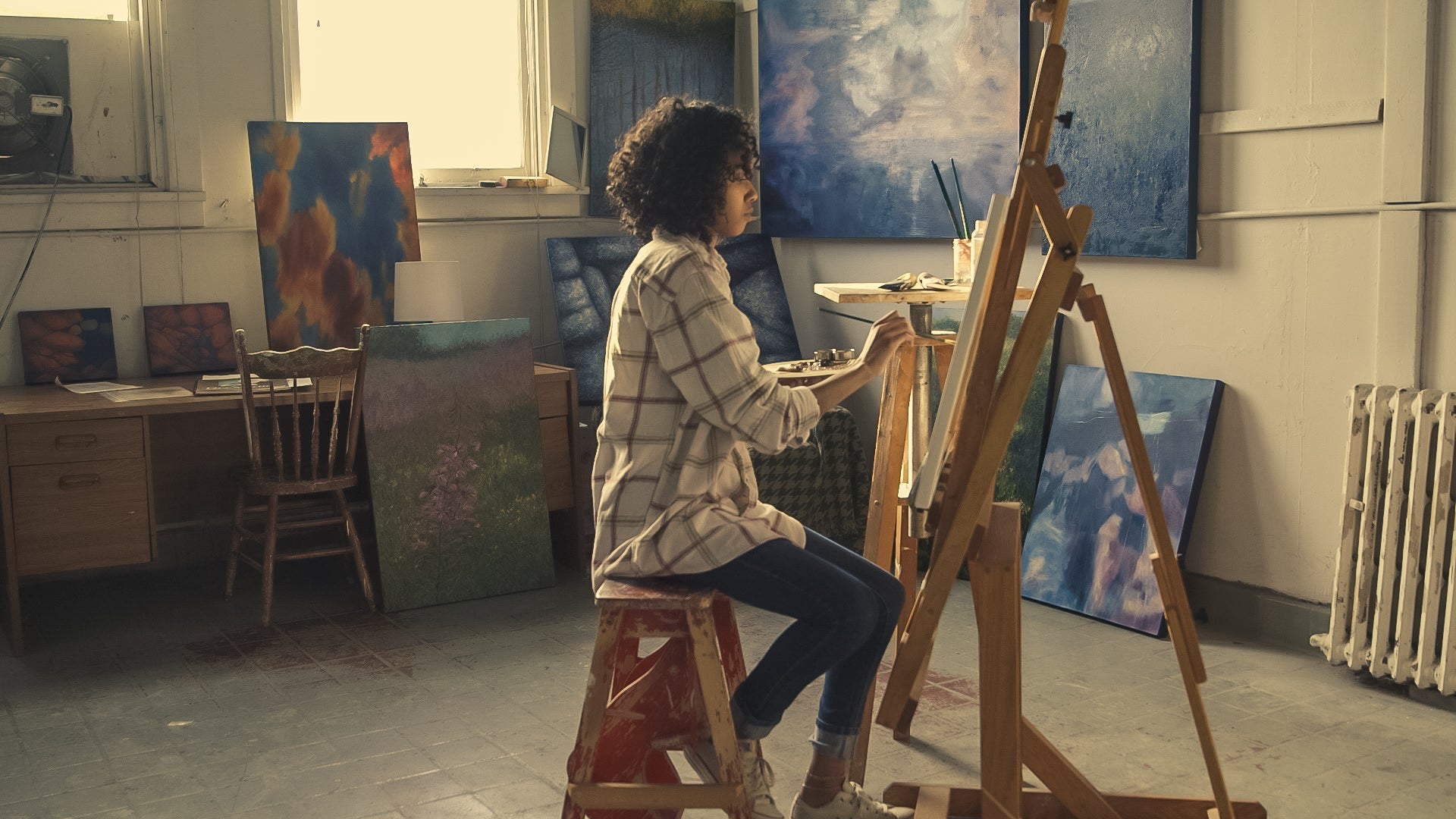 Painter working in an art studio surrounded by other pieces of finished art