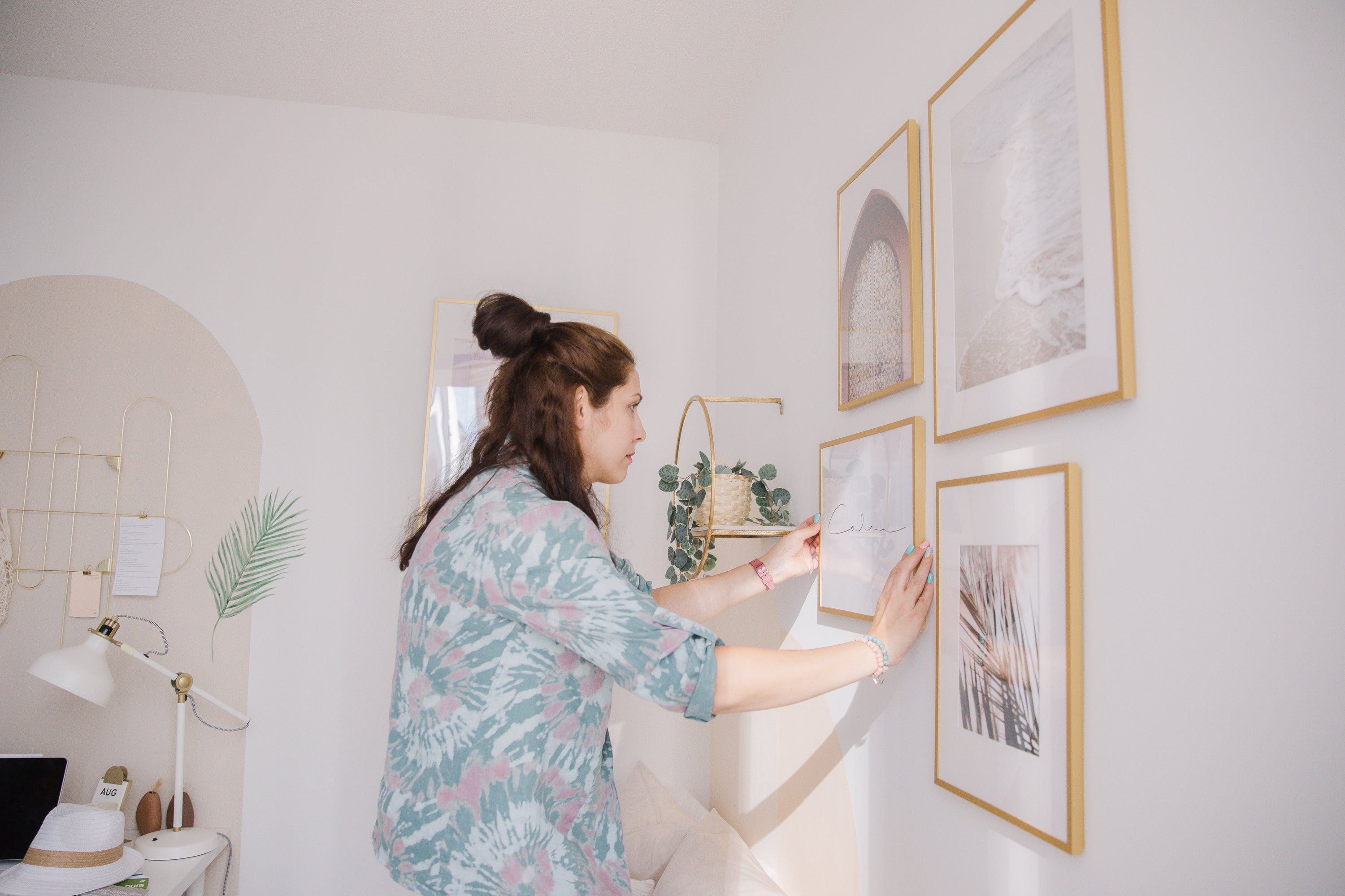 Person with long hair is hanging a wooden frame on a white wall.