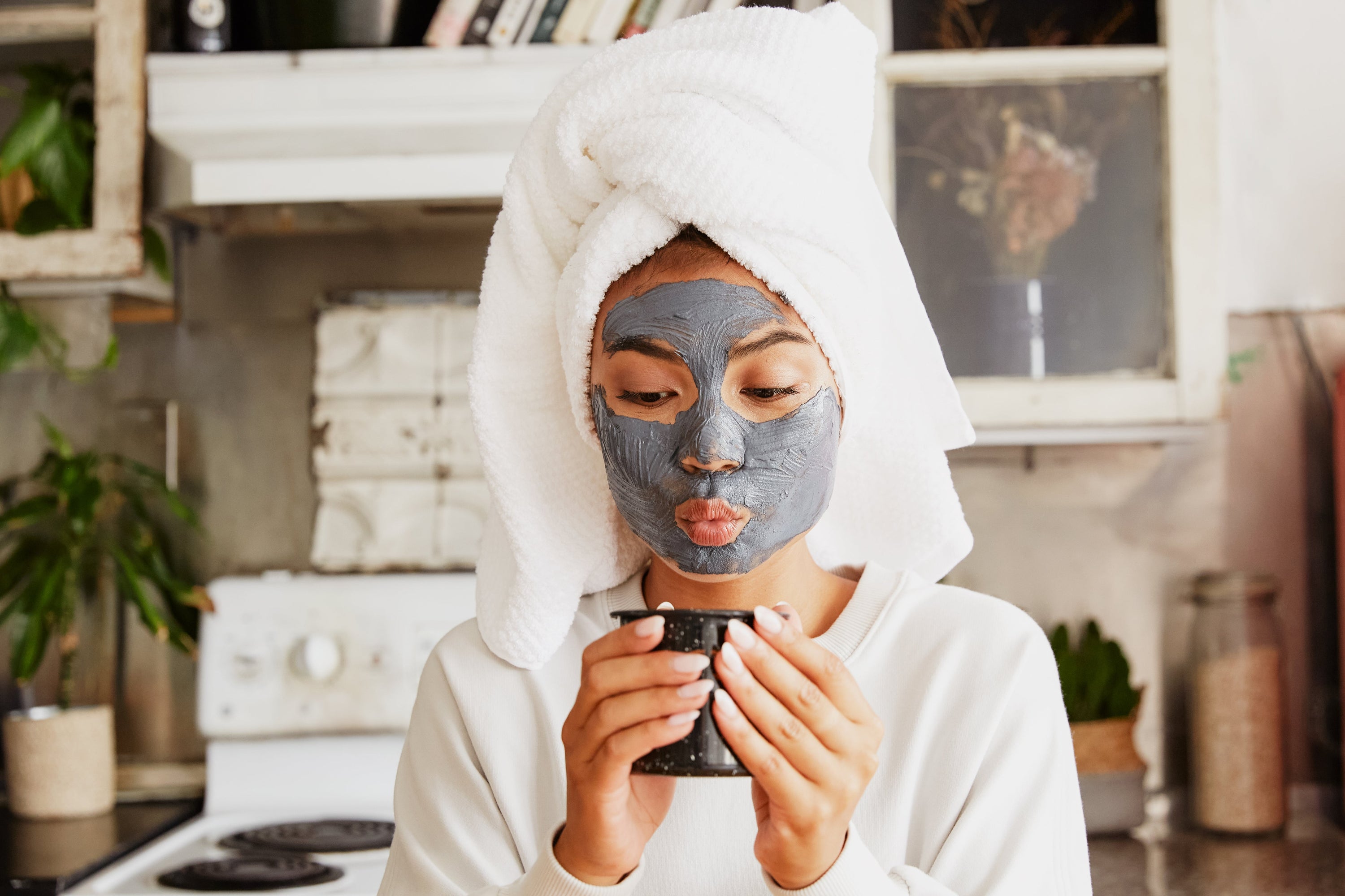 A young woman stands in her kitchen enjoying a nice hot drink as she completes her daily skincare routine.