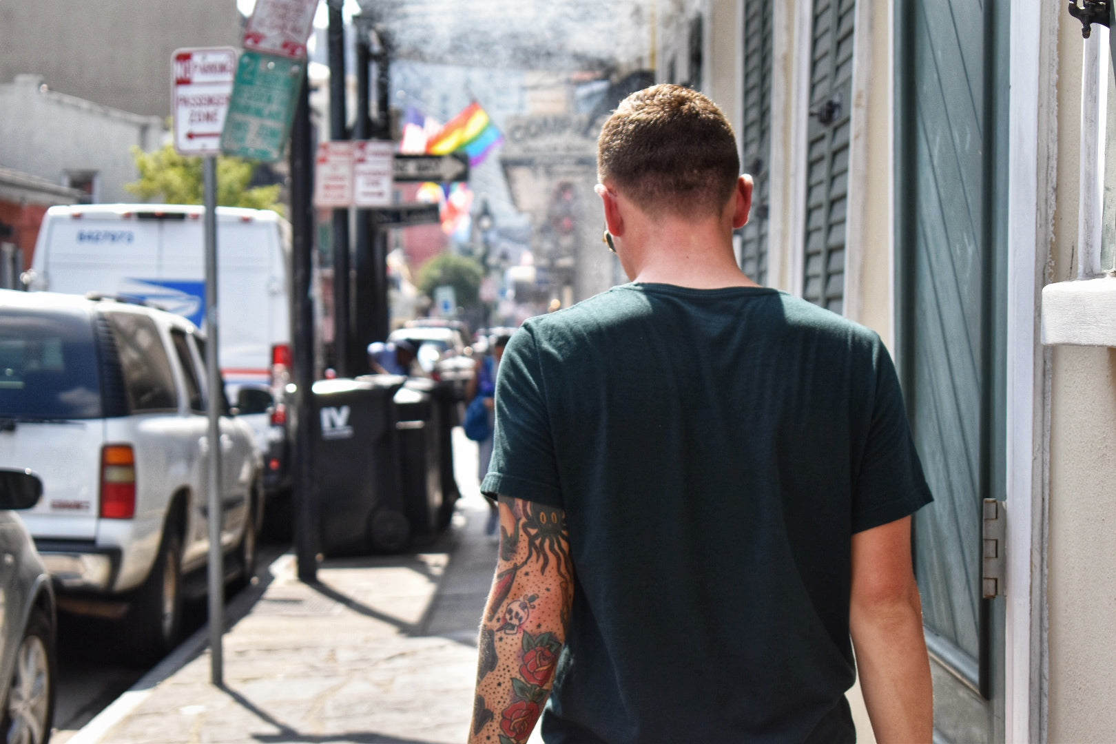 A man with tattoos covering his left arm takes a leisurely stroll through city streets in summer