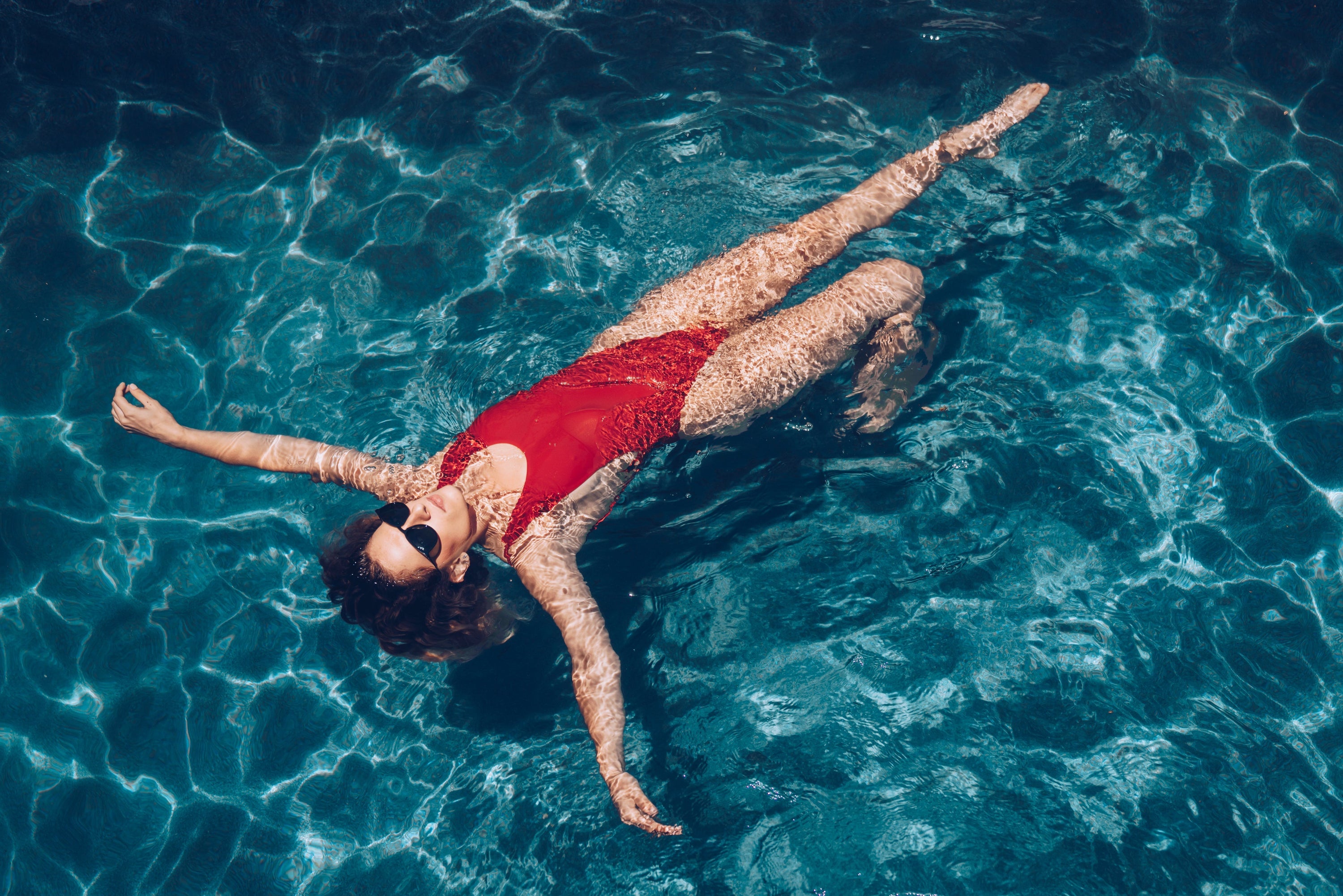 A woman floats on her back in the blue water of a pool.
