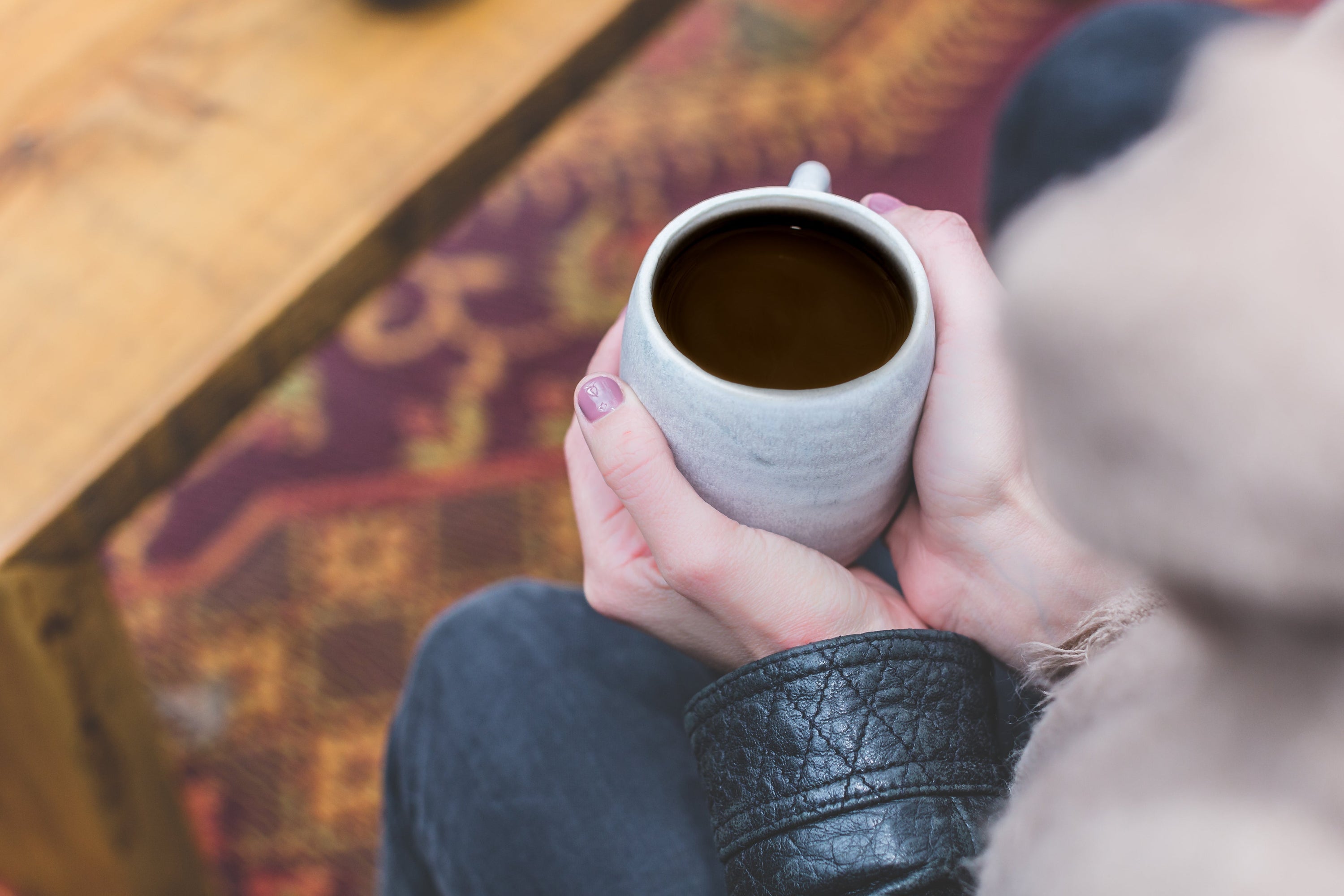 View looking down of a woman holding a light grey mug full of coffee.